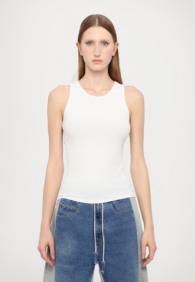 Débardeur blanc à côtes avec un col rond et sans manches. Associé à un jean en denim bleu avec une taille à cordon et des accents gris.