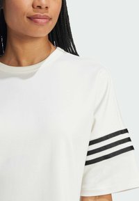 T-shirt bianco a maniche corte con scollatura rotonda, caratterizzato da tre stripe nere orizzontali sulle maniche superiori. Tessuto morbido.