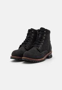 Botines de ante negro con punta redonda, diseño de cordones, herrajes de metal, costuras en contraste y suela de goma.