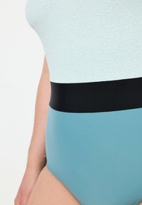 Maillot de bain une pièce avec une partie supérieure texturée bleu clair, une bande de section médiane noire et une partie inférieure bleu uni. Tissu lisse.