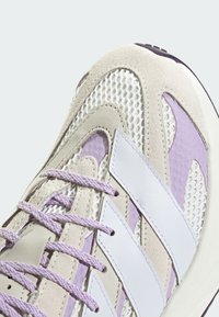 Fioletowe i białe sneakersy z siateczkową cholewką, akcentami z zamszu i teksturowaną gumową podeszwą. Sznurówki są jasnofioletowe, o eleganckim, nowoczesnym designie.