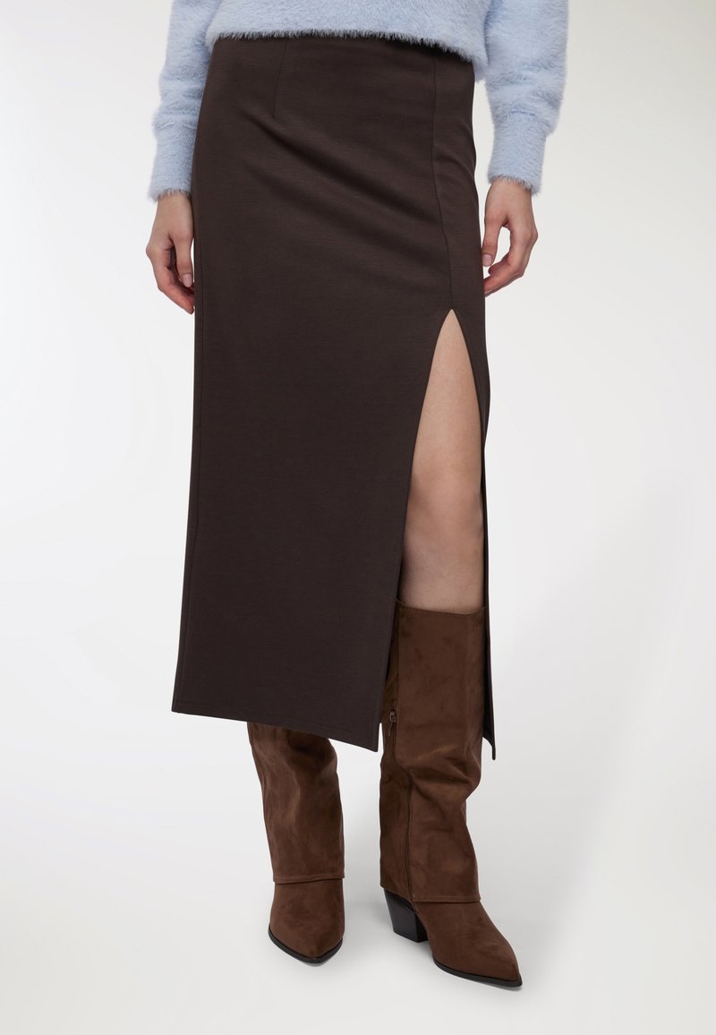 Donna che indossa una gonna midi marrone scuro con uno spacco vertiginoso abbinata a stivali con tacco in suede marrone e a un maglione morbido blu chiaro.