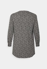 Svart långärmad blus med ett heltäckande mönster av små vita blommor, visad bakifrån.