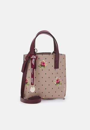Beige tote-taske med bikubemønster, spredte røde roser, burgunderfarvede håndtag, skulderrem og mærket bånd med rund metalkæde.