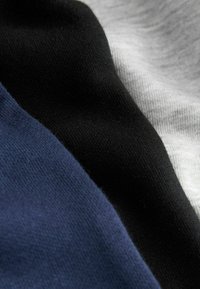 Gros plan sur un tissu plié bleu marine, noir et gris clair montrant une texture tricotée douce et un tombé fluide.