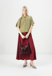 Olijfgroene shirt met korte mouwen, bordeaux maxi rok, bordeaux leren handtas met een gesp, en beige puntige slingback hakken.