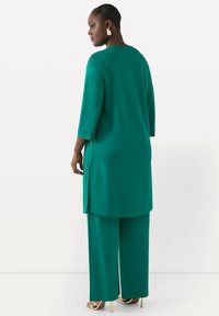 Teal tunika med trekvartärmar och sidslitsar, i kombination med vida byxor. Tyget verkar slätt med en matt finish.