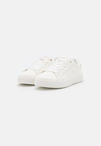 Hvite sneakers laget av glatt lær med en teksturert såle, med flate hvite snørebånd, subtile sømdetaljer og et minimalistisk design.