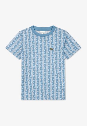 Lyseblå t-shirt med korte ærmer, prydet med et hvidt geometrisk mønster og en lille grøn Lacoste-logo på brystet. Fremstillet i bomuld.