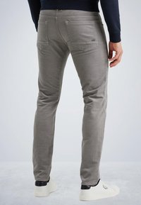 Pantalones gris ajustados con cinco bolsillos, costuras sutiles y detalle del logo en el bolsillo trasero. Combinados con zapatillas blancas.