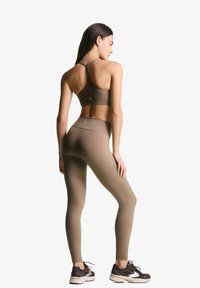 Brun sportsbh og leggings lavet af strækbart stof. Bh'en har et racerback-design; leggingsene har en høj talje og en tætsiddende silhuet.