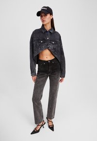 Chaqueta de denim negra recortada con grandes bolsillos, cierre de botones y dobladillo sin rematar. Combinada con unos pantalones vaqueros negros de cintura alta y tacones altos negros.