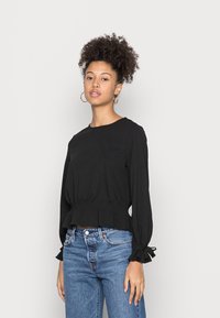 Black, long-sleeve top with a cinched waist and gathered sleeves. Paired with light blue high-waisted jeans. Simple design and smooth texture.