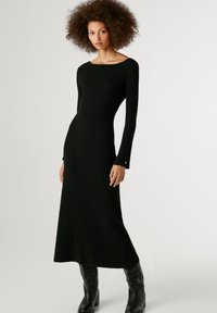 Juoda gample nėriniuota suknelė su valsčiaus iškirpte, ilgomis prigludusiomis rankovėmis ir tiesia siluetu. Yra mažas mygtuko akcentas ant rankovės.