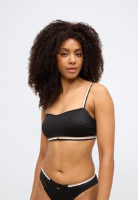 Σετ μαύρου μπικίνι με τοπ στυλ bandeau με λεπτές τιράντες και αντίθετο περίγραμμα. Το ύφασμα φαίνεται λείο με ελαφριά υφή.