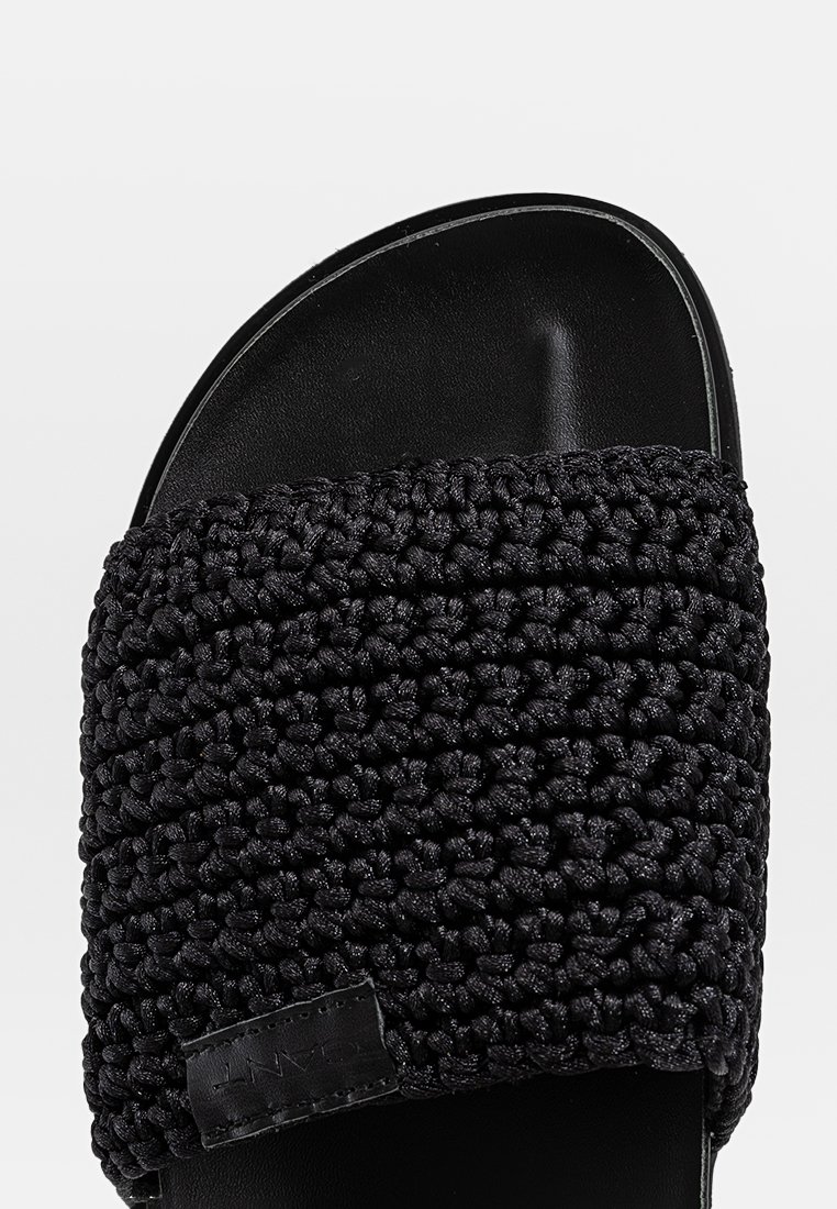 Czarne klapki z teksturowanym, plecionym paskiem i gładką czarną podeszwą. Pasek ma przymocowaną metkę, prezentującą starannie wykonany design.