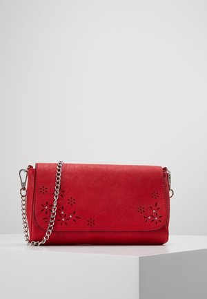 Clutch de cuero rojo con patrones florales recortados y pequeños cristales, con una correa de cadena plateada y cierres metálicos sobre una superficie blanca.