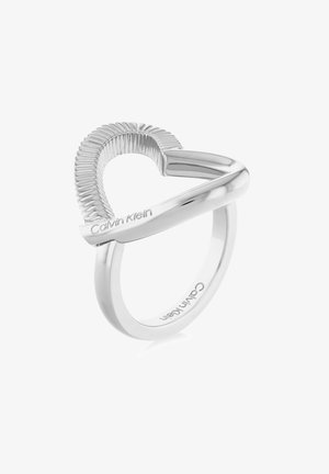 Bague argentée Calvin Klein avec une forme de cœur partiellement nervurée et le nom de la marque gravé sur une bande lisse.