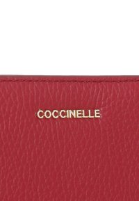 Rode leren portemonnee met een gestructureerde afwerking, voorzien van een gouden "Coccinelle" logo. Het ontwerp is compact met zichtbare stiksels.