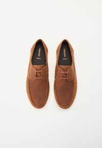 Hnedé kožené topánky s okrúhlou špičkou, šnurovací dizajn a kontrastná biela podrážka. Šitie zdôrazňuje okraje. Značka je viditeľná vo vnútri.