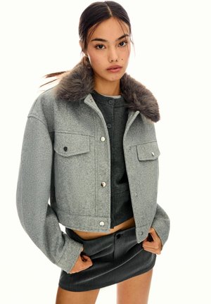 Grijze cropped jack van textuurstof met een faux fur kraag, voorzien van twee voorzakken en drukknopen. Gepaard met een grijze top en rok.