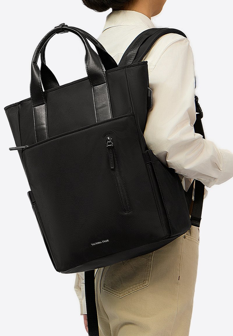 Czarny plecak wykonany z teksturowanej tkaniny z gładkimi skórzanymi akcentami, wyposażony w podwójne górne uchwyty i regulowane paski oraz przednią kieszeń na zamek.