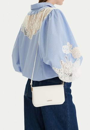 Persona che indossa una blusa a righe blu con dettagli in pizzo bianco, jeans scuri e una piccola borsa a tracolla bianca Lasocki.