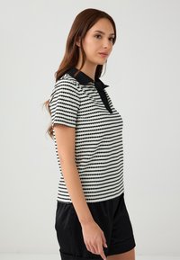Zwart-wit gestreepte polo met korte mouwen, een zwarte kraag en een textuurstof. Gepaard met zwarte shorts.