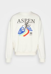 Sudadera cremosa con un corte relajado, que presenta un gráfico colorido de un esquiador y montañas. Con el texto "ASPEN" acentuado en la parte superior.