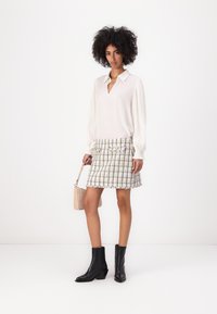 White blouse with pleated sleeves, paired with a multicolored tweed skirt. Black ankle boots and a small beige handbag complete the outfit.