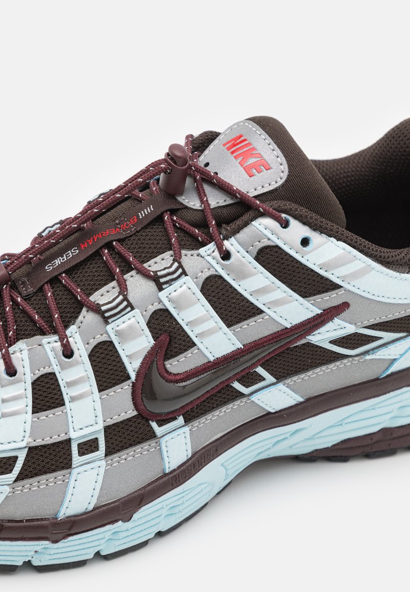 Chaussure de course Nike en marron, gris et bleu clair. Comprend une tige en mesh respirant, des superpositions à motifs et des accents de logo bien visibles.