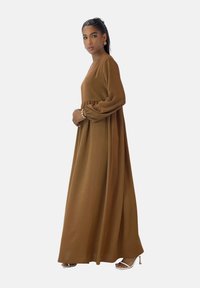 Braunes lang�ärmliges Maxikleid mit tailliertem Bund, aus weichem Stoff. Verfügt über einen V-Ausschnitt und einen fließenden Rock. Trägt silberne Accessoires.