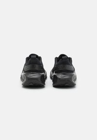 Een paar zwarte Nike sportschoenen gezien vanuit de achterkant, met textuur op de zolen en trekbandjes tegen een effen witte achtergrond.