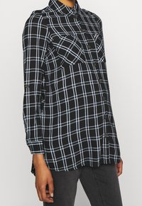 Svart och blå rutig skjorta med långa ärmar, knappstängning fram, två bröstfickor, rundad nederkant och mjuk tygkvalitet.