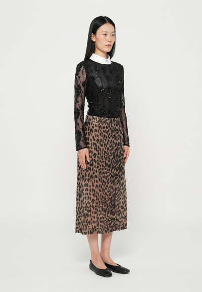 Haut noir à manches longues en perles avec une texture transparente, associé à une jupe midi à imprimé léopard marron. Des ballerines noires complètent la tenue.