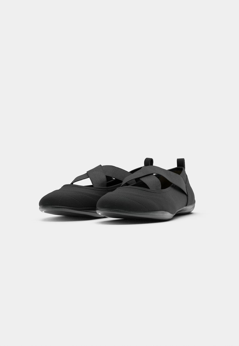 Ein Paar schwarze Slipper mit gekreuzten elastischen Riemen und Zugschlaufen vor einem sauberen weißen Hintergrund.