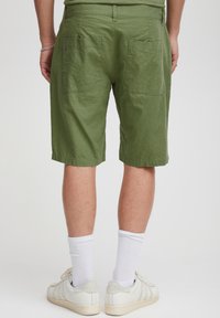 Žalios spalvos lininės šortai laisvo silueto, su dviem kišenėmis gale. Dėvimi su baltais kojinėmis ir šviesios spalvos sportbačiais.