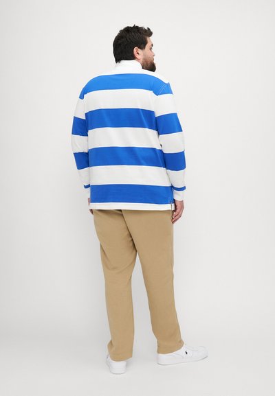 Stripet langermet skjorte i blått og hvitt, med en løs passform og sidesplitter, sammen med lyse beige bukser og hvite sneakers.