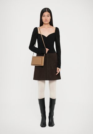 Haut noir à manches longues avec texture froncée, jupe en daim marron, collants crème et bottes noires jusqu'aux genoux. Sac à main beige avec bandoulière.