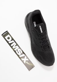 Black athletic shoe with a textured mesh upper, round toe, and lace-up design. Includes a branded tag with a geometric pattern in black and gold.