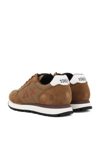 Sneakers in suede marrone con un design accentuato caratterizzato da simboli geometrici rossi. I dettagli del tallone bianchi includono l'anno "1968" e una suola nera.