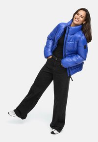 Blue puffer jacket with a high collar and ribbed cuffs, paired with black wide-leg pants and white sneakers. Smooth, glossy texture.