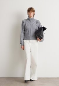 Siva pletena turtleneck jopica z ribjastimi detajli, v kombinaciji z belimi širokimi hlačami. Model drži črno teksturirano torbico.
