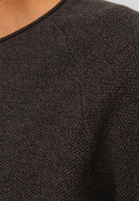 Bruine gebreide trui met een ronde halslijn, textuurstof en subtiele stikdetails langs de schoudernaad.