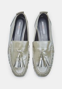 Mocassins en cuir vert olive avec une texture crocodile, des franges décoratives et un détail de couture. Doublure intérieure noire et étiquette visibles.