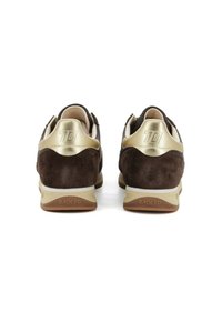 Un par de zapatillas de ante marrón y doradas vistas desde atrás, con "70" grabado en la etiqueta del talón dorado y "BACK 70" en las suelas beige.