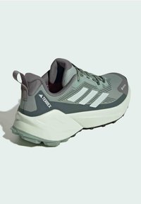 Zelená a šedá sportovní bota s texturovaným svrškem, bílými pruhy, polstrovaným límcem a profilovanou podrážkou pro trakci. Obsahuje poutko na patě.