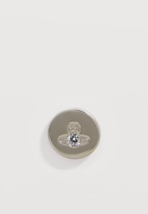 Pulsante rotondo in argento con un disegno inciso a forma di anello e una pietra preziosa trasparente e scintillante al centro su sfondo bianco.