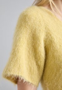 Suéter de mezcla de mohair amarillo con mangas cortas y anchas. Texto suave y forma voluminosa, con un acabado ligeramente borroso en el dobladillo.