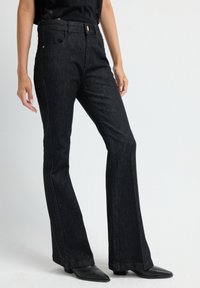 Zwarte denim flare jeans met vijf zakken, gouden hardware en een soepele textuur. Gecombineerd met puntige zwarte schoenen.